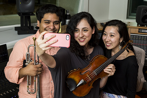 Musicians pose with their instruments for a selfie in a recording studio on campus